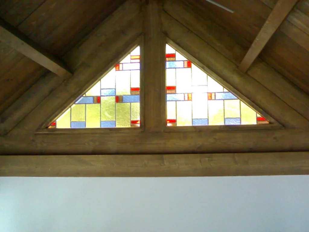 Driehoekig geometrisch glas-in-loodraam in een dakvlak, rood-blauw-amberpatroon